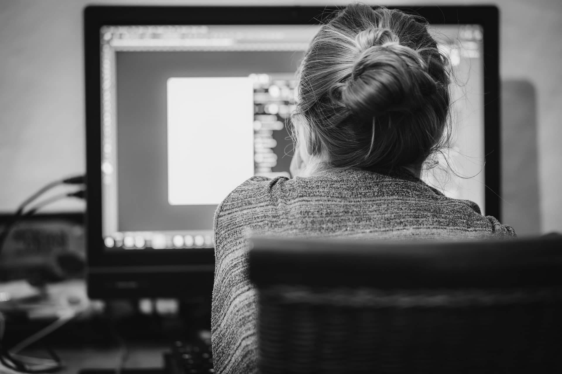 Black-and-white photo from behind a woman at her home-office computer