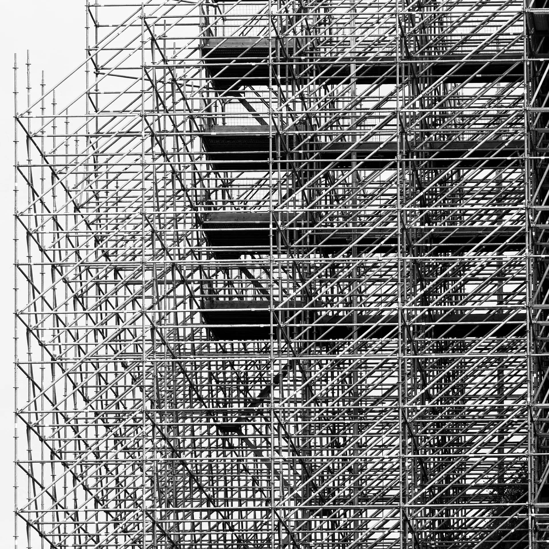 Black-and-white photo of construction scaffolding rising against a pale sky